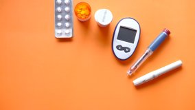 Insulin pen, diabetic measurement tools and pills on orange background.